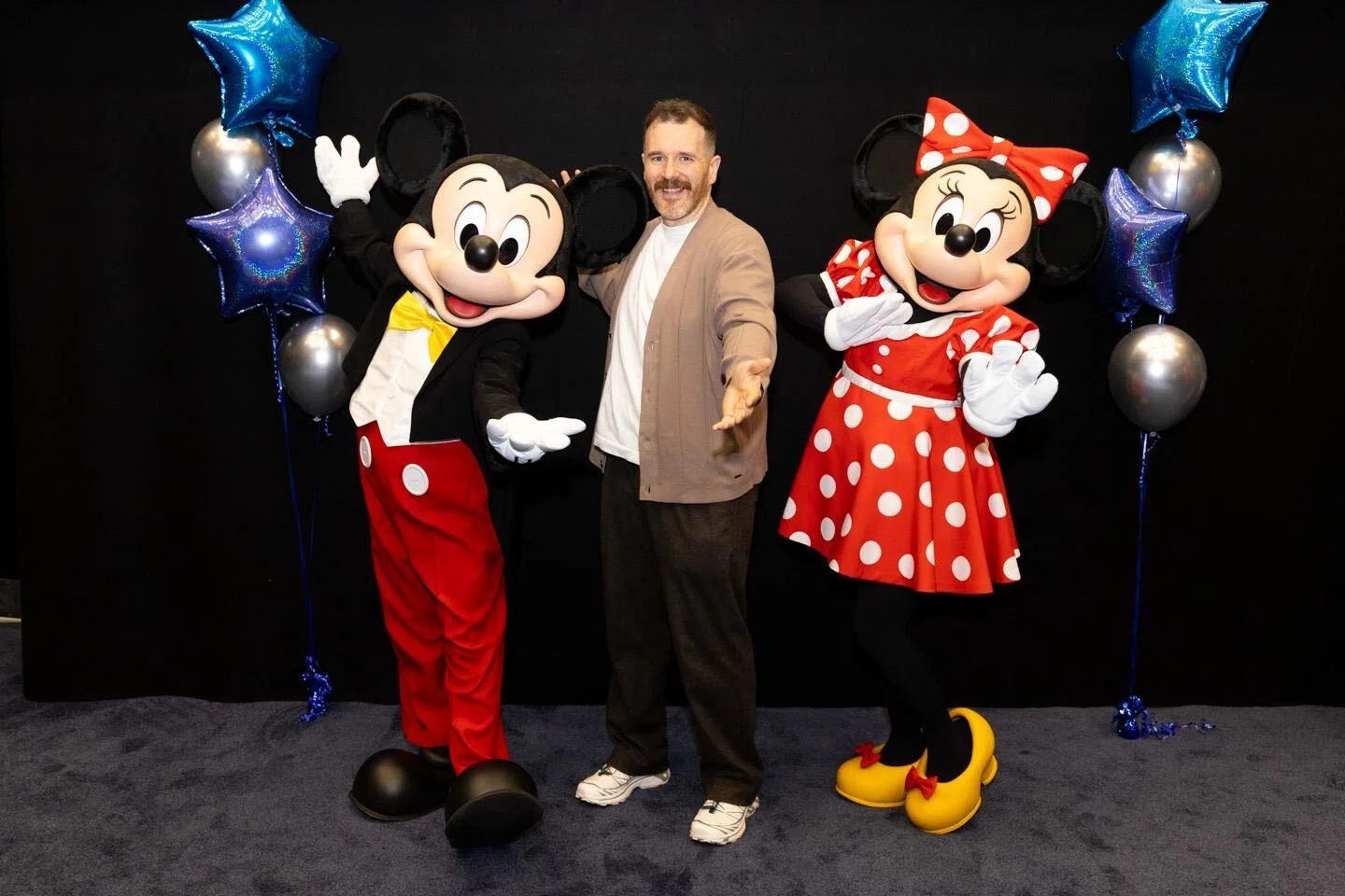 Mickey and Minnie Mouse posing with a man in front of blue and silver balloons